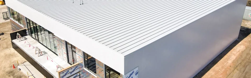 A sleek new commercial building. The building is rectangular and features white metal siding, with a matching white metal roof.