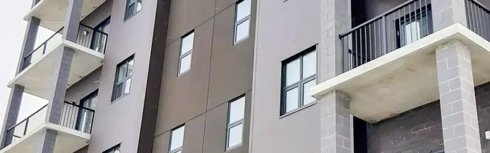 A modern six-story apartment building, with a mixture of brick walls and metal siding. It features multiple balconies supported by brick columns.