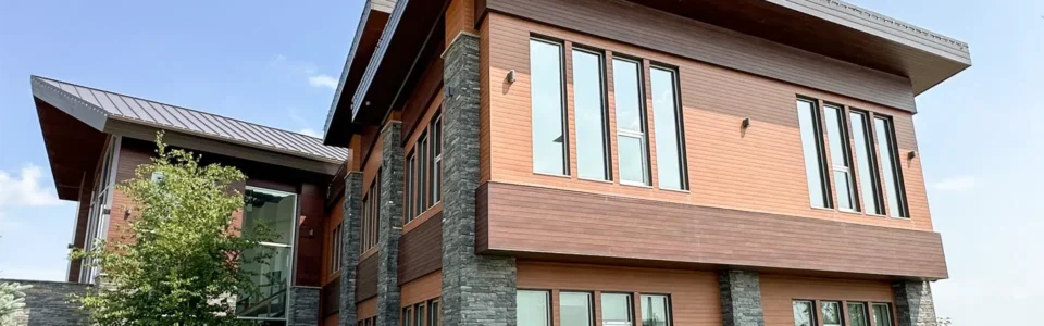 A modern two-story building in Winnipeg, Manitoba. The building has orange and brown wood-textured metal siding and soffits, with stone accents and a sloped metal roof.